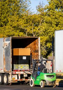 Red semi-truck hauling wooden crates on a highway under a blue sky with trees.