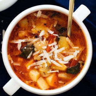 Close-up of minestrone soup in a white bowl, garnished with grated cheese.