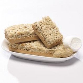 Three peanut butter crumble bars on a white plate with a peanut and a dollop of cream.