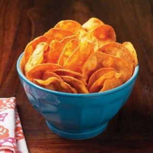 Blue bowl overflowing with orange potato chips on a wooden table.