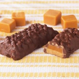Chocolate-covered caramel candy bars with caramel cubes on a yellow and white striped surface.