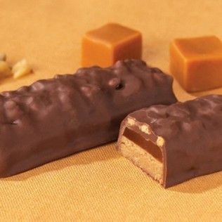 Chocolate-covered candy bars with caramel filling, alongside caramel cubes on an orange surface.