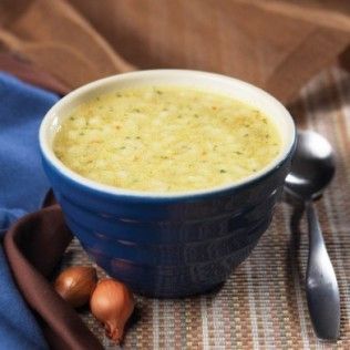 Blue bowl of creamy soup with a spoon, onions, and a blue napkin on a table.