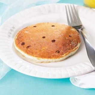 Pancake with chocolate chips on a white plate, next to a fork.