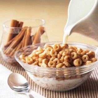 A bowl of cinnamon cereal being poured with milk, with a jar of cinnamon sticks beside it.