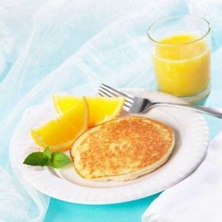 Pancake on a plate with orange slices, mint, and orange juice.