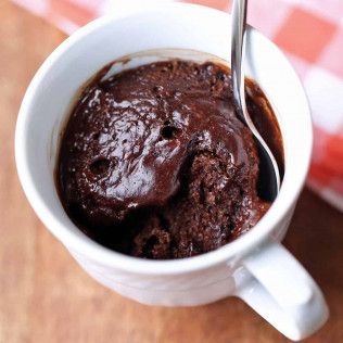 Chocolate mug cake in a white mug with a spoon inside, on a wooden surface.