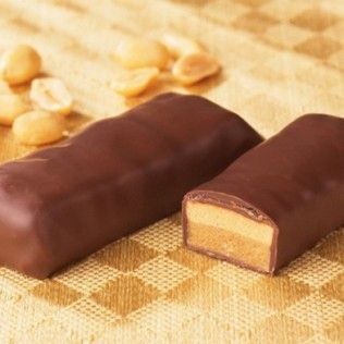 Chocolate-covered candy bars with a peanut butter filling, placed on a gold-checkered surface with peanuts scattered around.