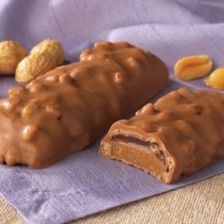 Two peanut butter candy bars coated in caramel, with peanuts scattered.