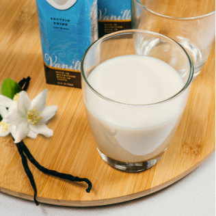 Glass of vanilla protein drink on wooden tray with vanilla bean and flowers.