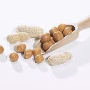 Peanuts and peanut candies spilling from a wooden scoop, with peanut shells scattered.