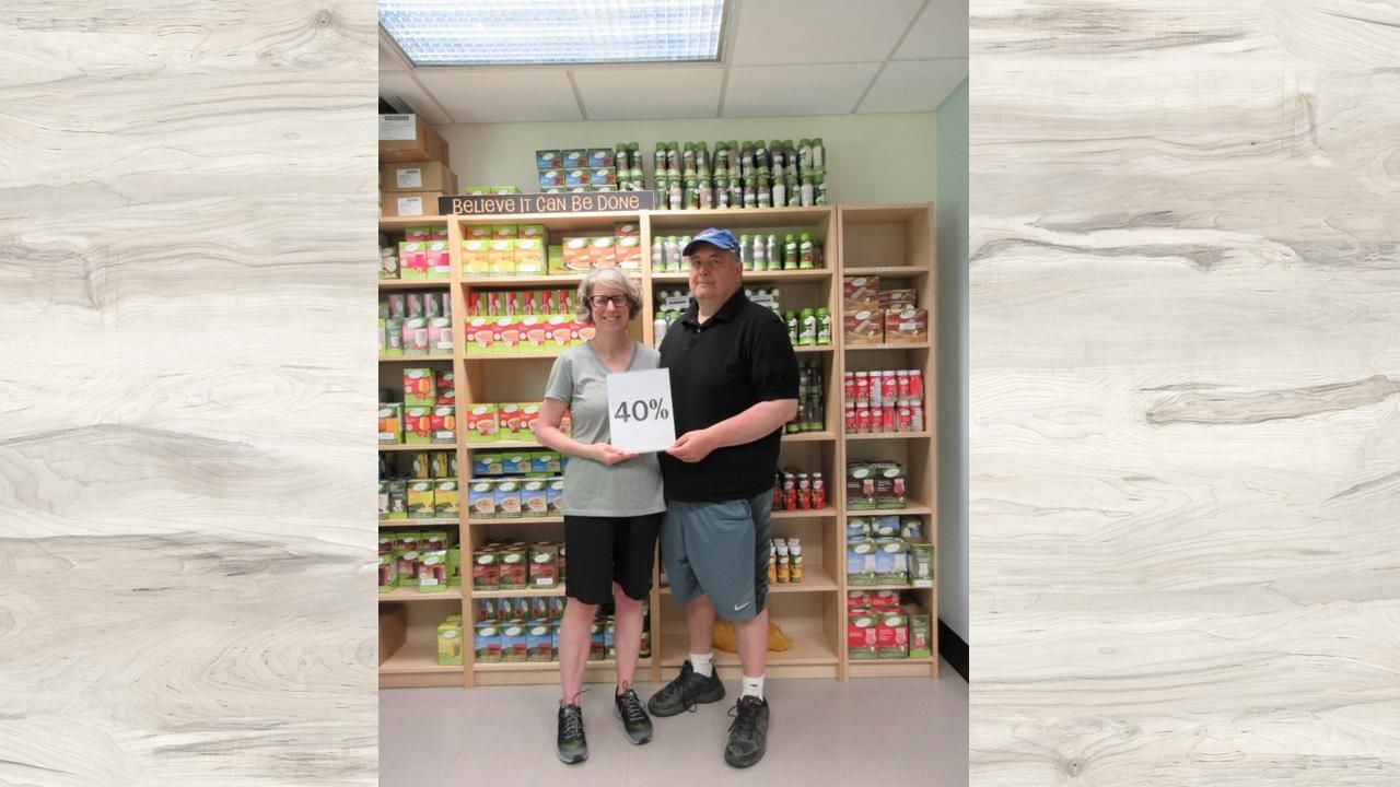 Two people standing in a store aisle, holding a sign in front of shelves stocked with colorful products.