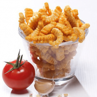 Bowl of orange, crinkle-cut snacks, with a tomato and garlic on a white surface.