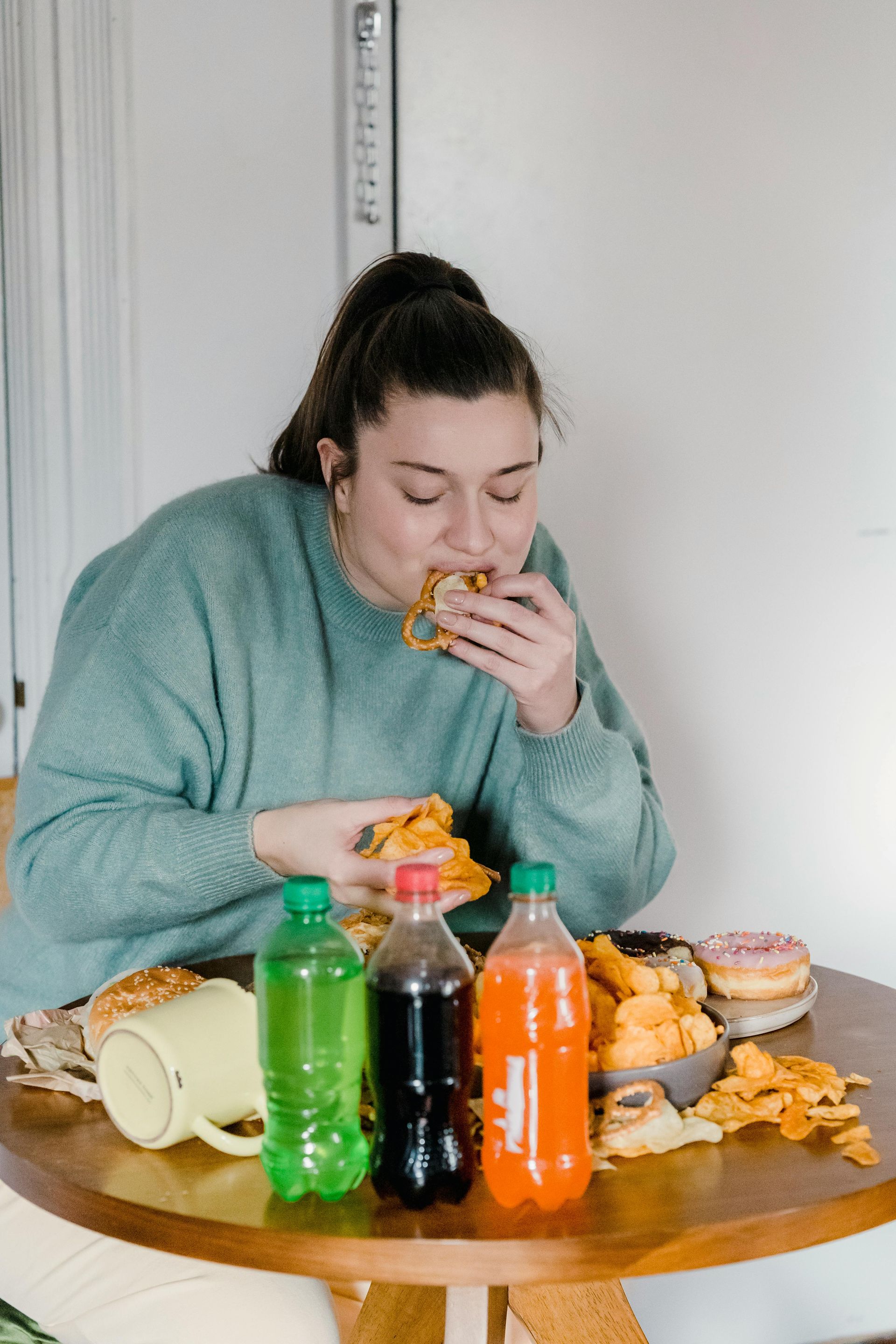 Woman eating burger at table with snacks and soda.