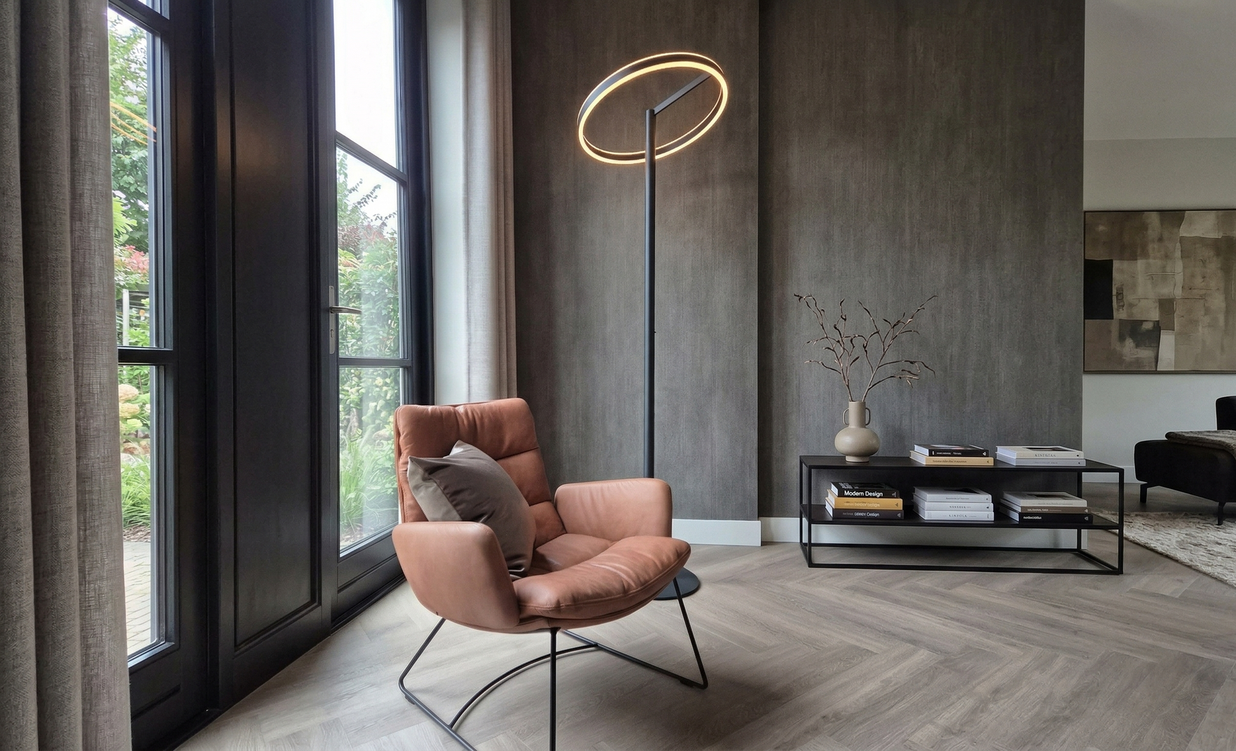 In een kamer met een grijze muur met structuurverf en een visgraatparketvloer staat een leren fauteuil naast een hoge.