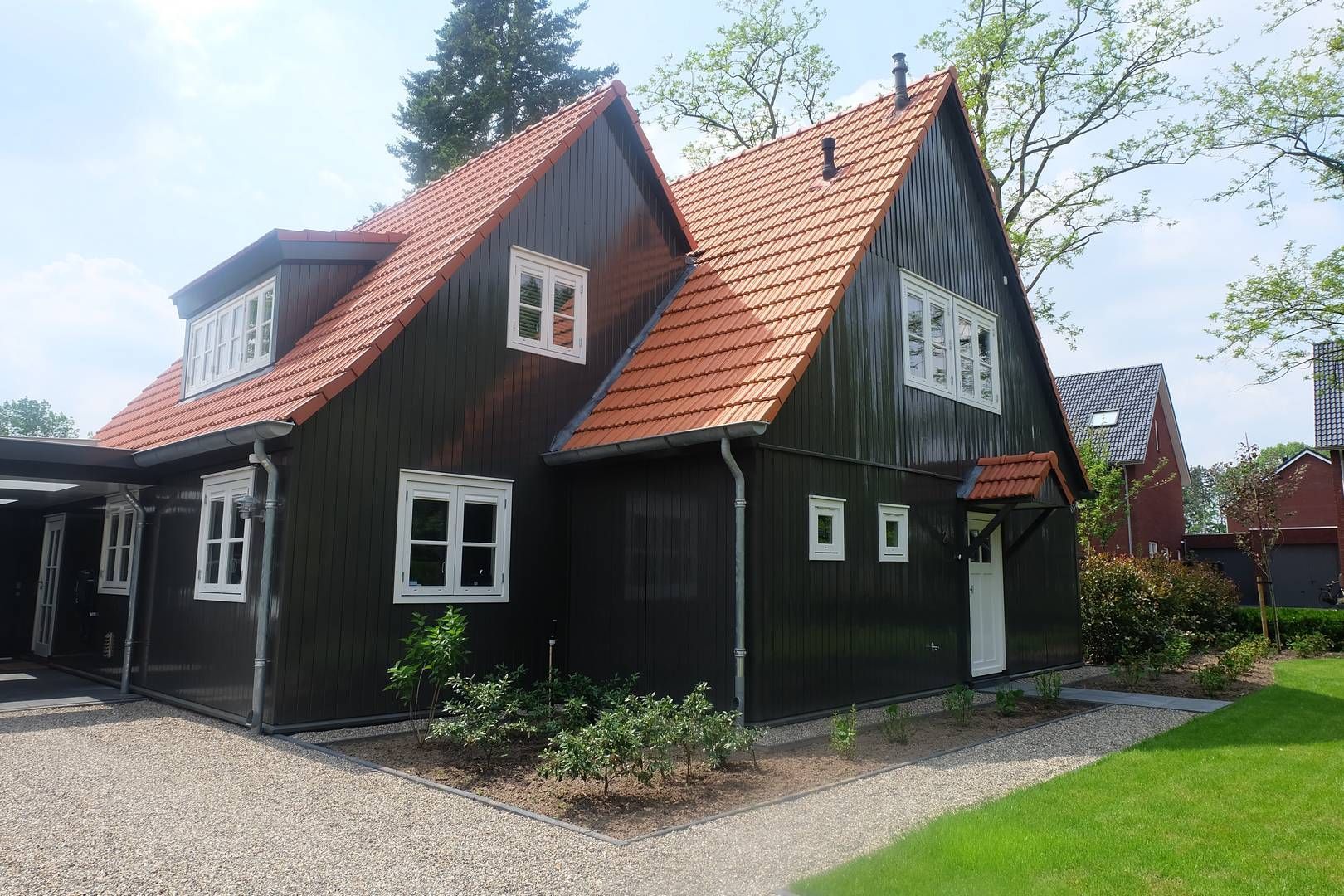 Een witte boerderij met een rieten dak, donkere dakpannen en dakramen staat achter een groen gazon en een terras.