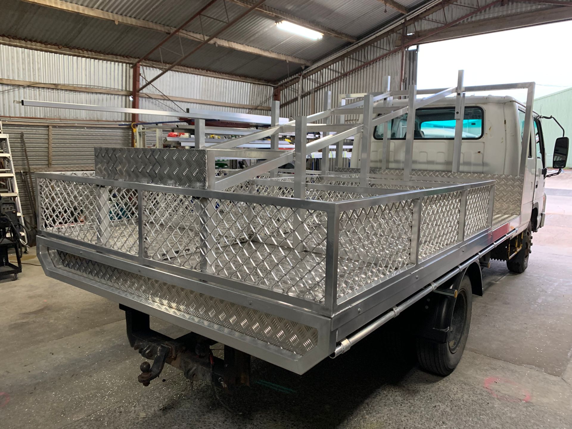 White flatbed utility truck with aluminum cage sides parked inside a warehouse — Jensen Welding & Fabrication in Chevallum, QLD