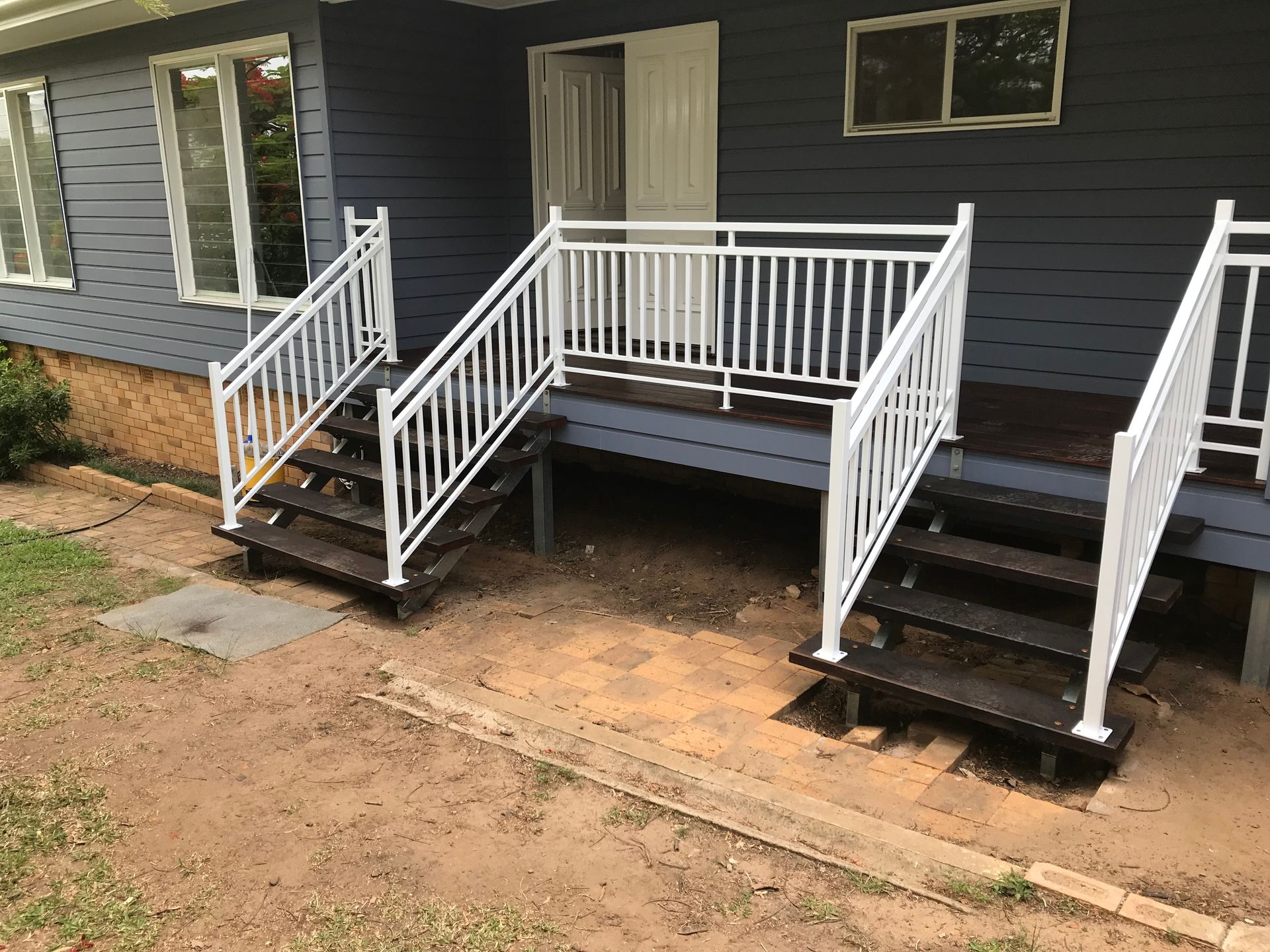 Front porch with white railings and dark steps on a gray house, with a small walkway and dirt yard. — Jensen Welding & Fabrication in Chevallum, QLD