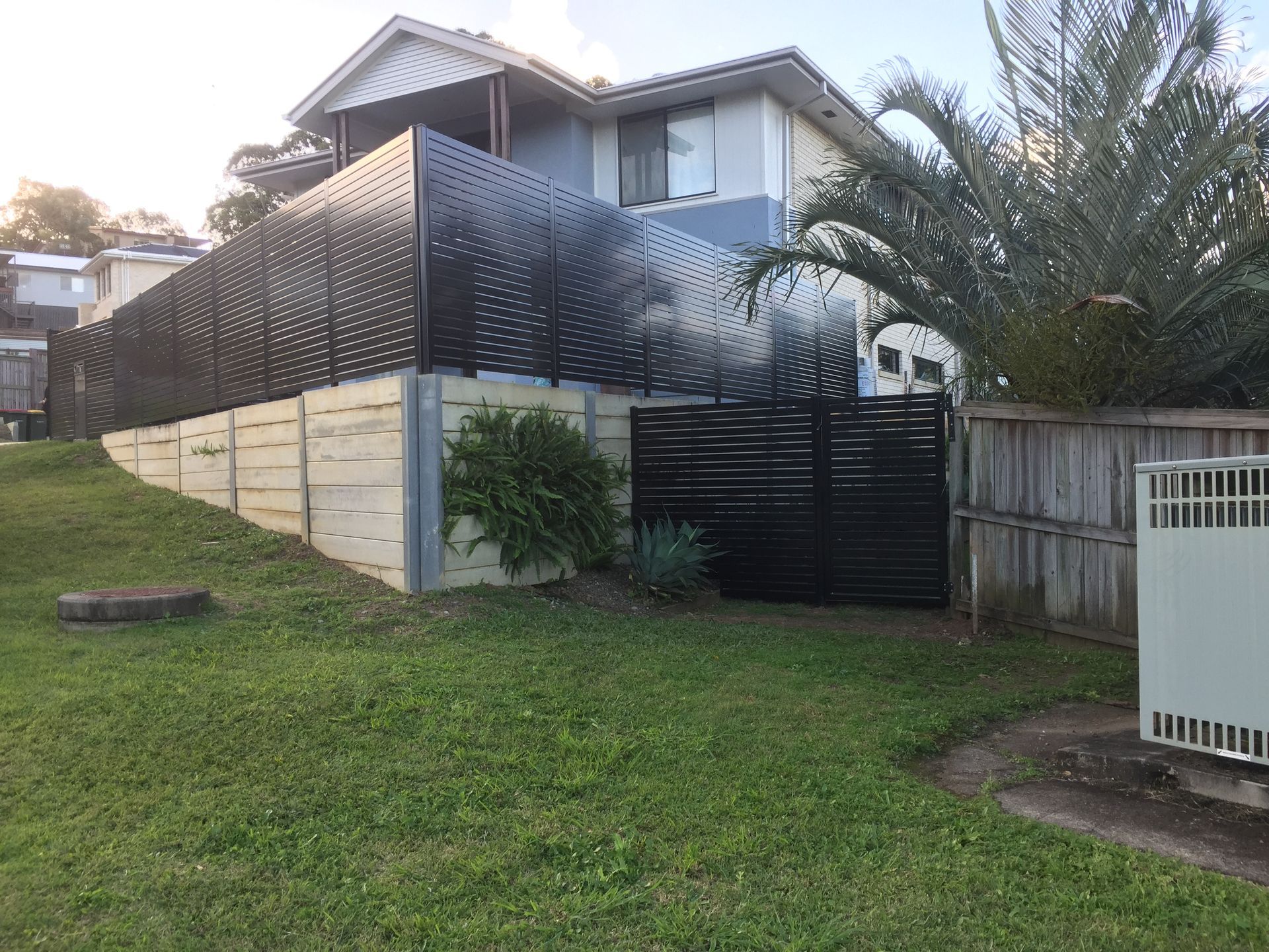 Suburban house with black privacy fence, driveway gate, and grassy front yard on a hill  — Jensen Welding & Fabrication in Chevallum, QLD