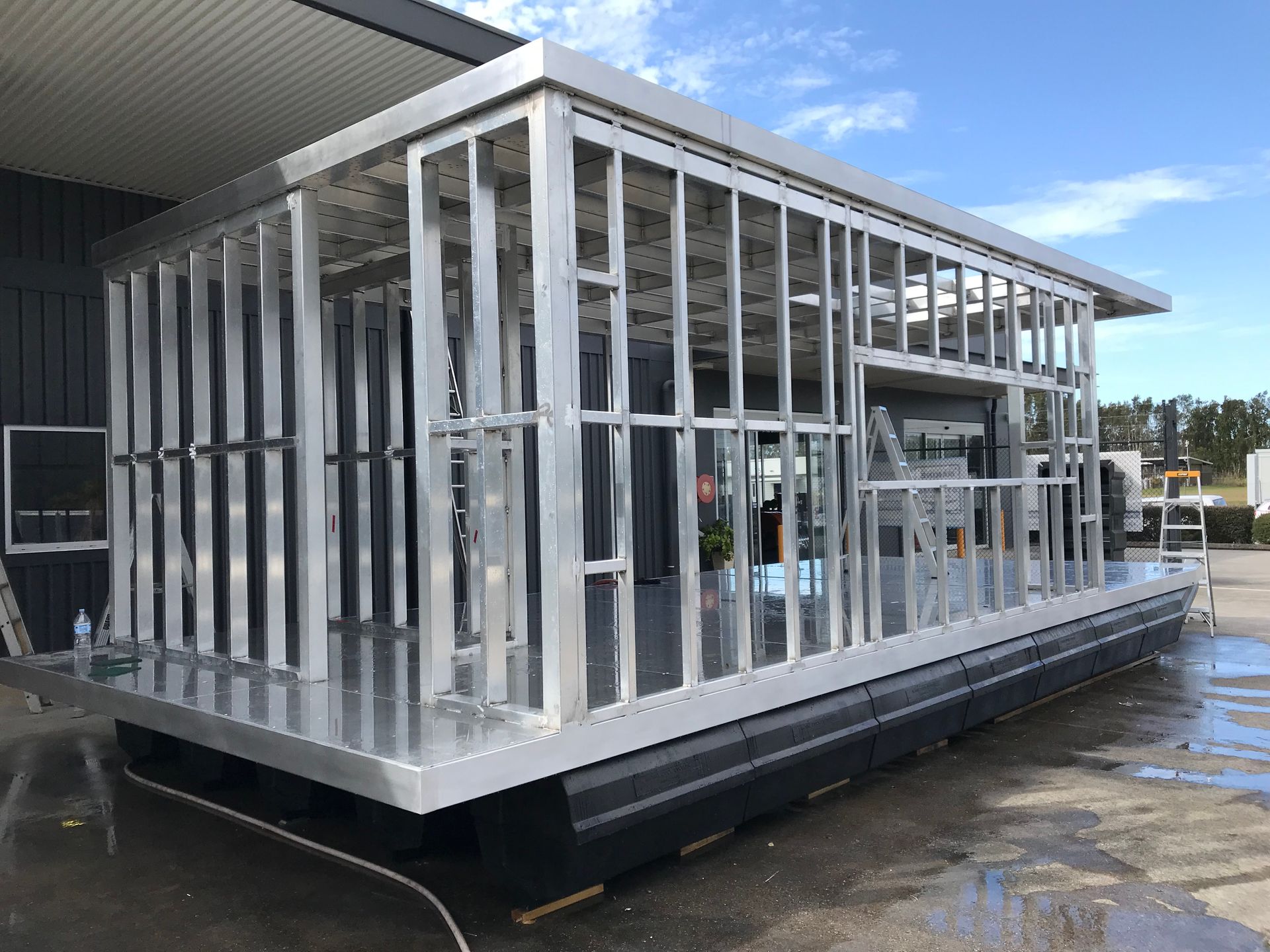 Metal-framed modular structure on a black floating platform beside a building, under construction  — Jensen Welding & Fabrication in Chevallum, QLD