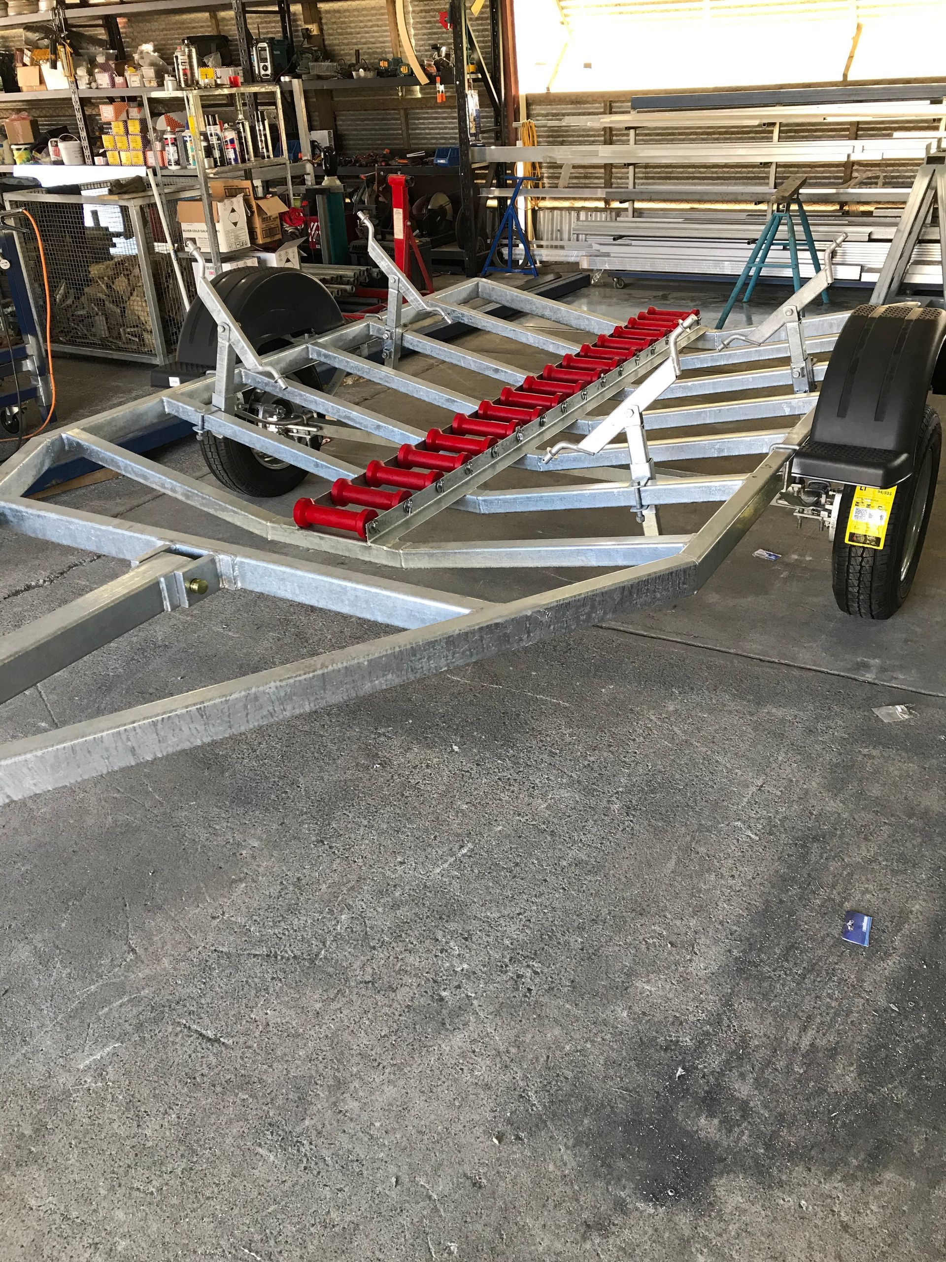 Boat trailer with red rollers parked in a workshop garage  — Jensen Welding & Fabrication in Chevallum, QLD