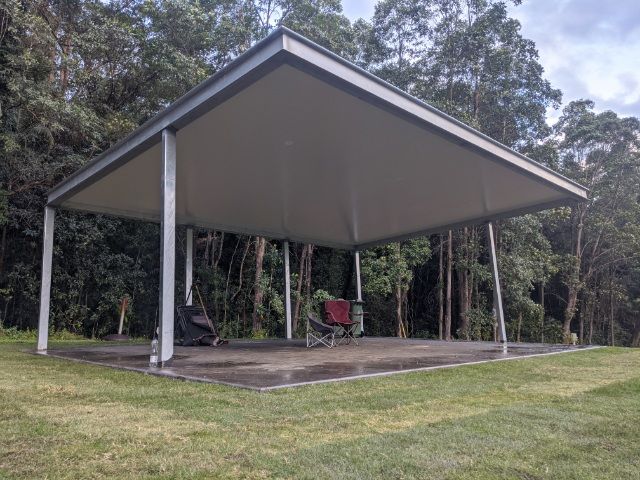 Open-sided pavilion with a metal roof and a few chairs in a grassy park clearing — Jensen Welding & Fabrication in Chevallum, QLD