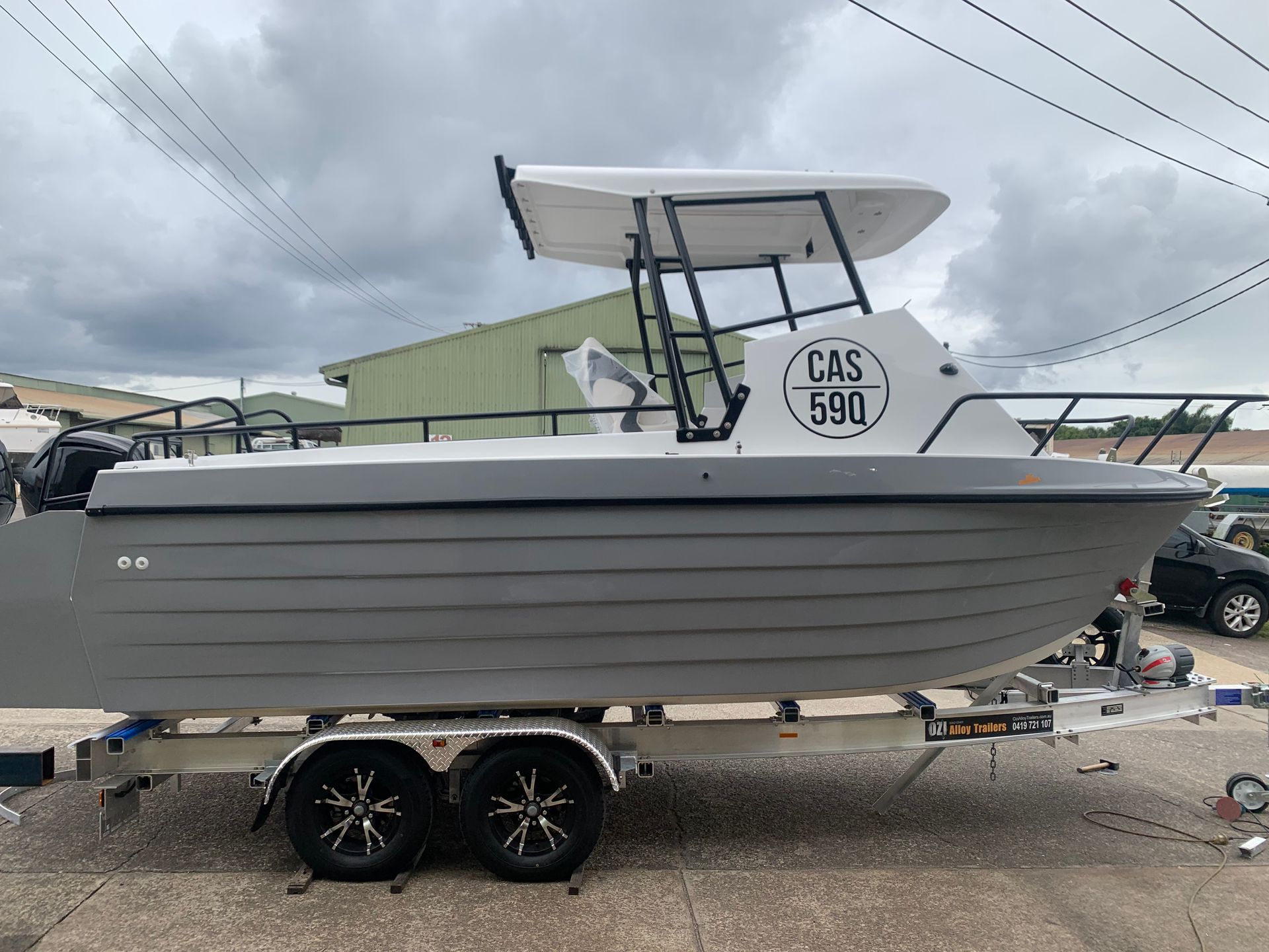 White motorboat on trailer, side view, with gray stripe and canopy in a boat yard under cloudy skies — Jensen Welding & Fabrication in Chevallum, QLD