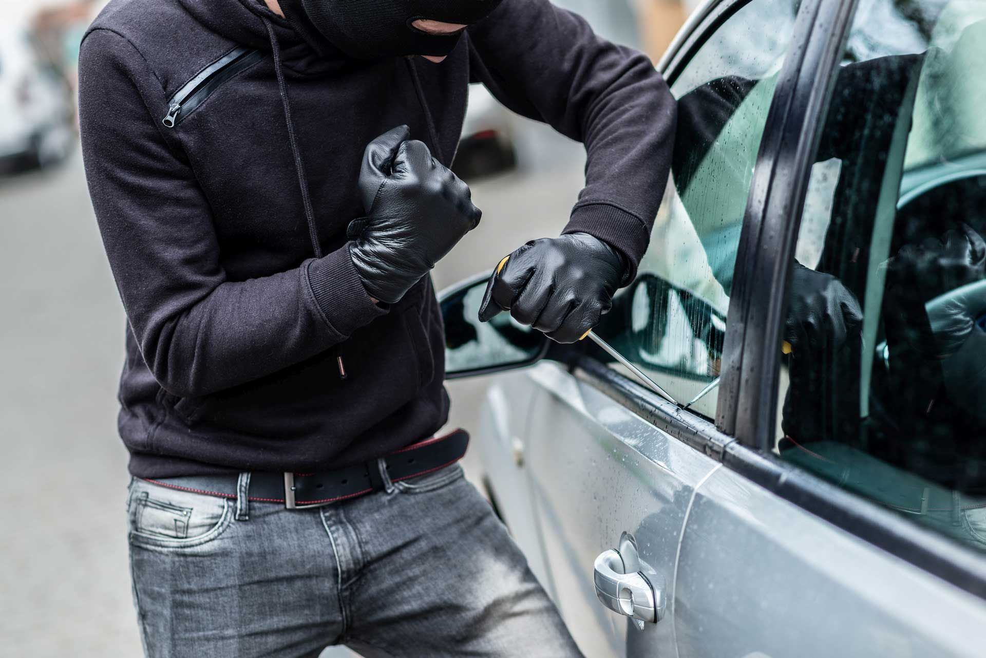 A man in a mask is trying to break into a car.