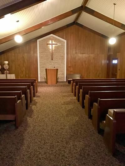 Empty church sanctuary with wooden pews, central aisle, and cross above the altar at the front