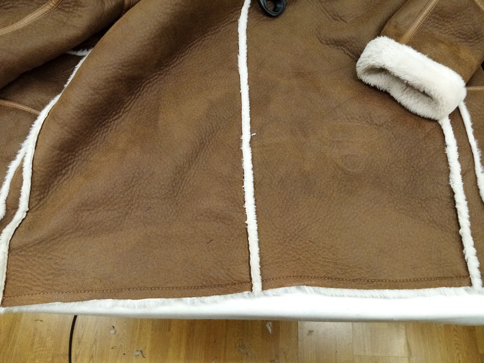 Une veste marron avec une bordure blanche est posée sur une table en bois.