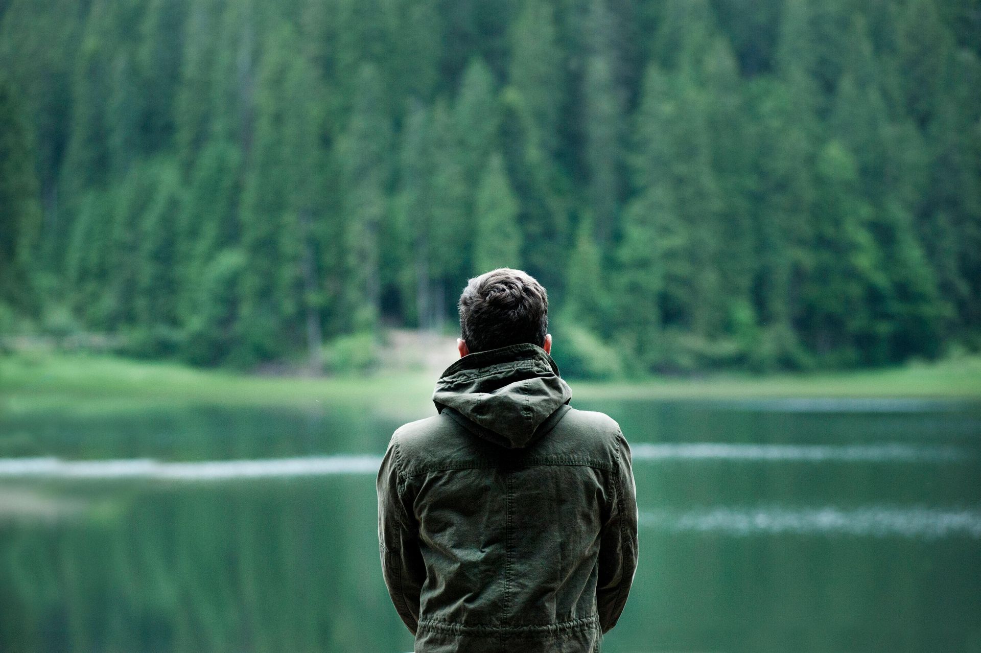 Un homme se tient devant un lac avec des arbres en arrière-plan.