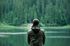 Un homme se tient devant un lac avec des arbres en arrière-plan.
