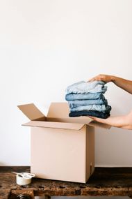 Une personne tient une pile de vêtements dans une boîte en carton.