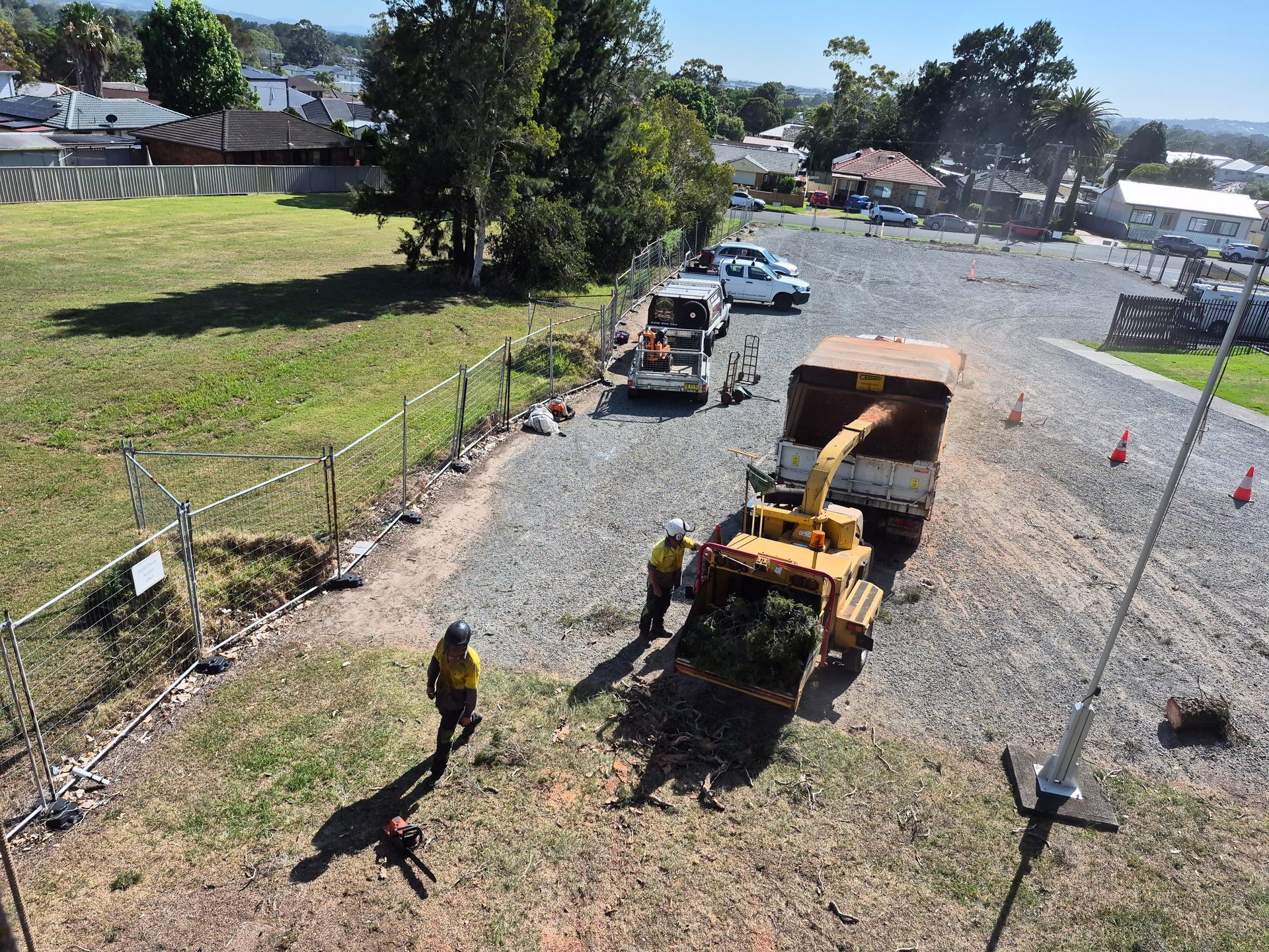Workers chipping brush near a road. Two men in safety vests operating machinery on a gravel area.