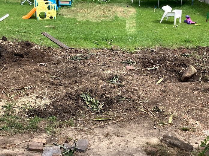 A bare garden bed with exposed soil, surrounded by grass and a children's play area.