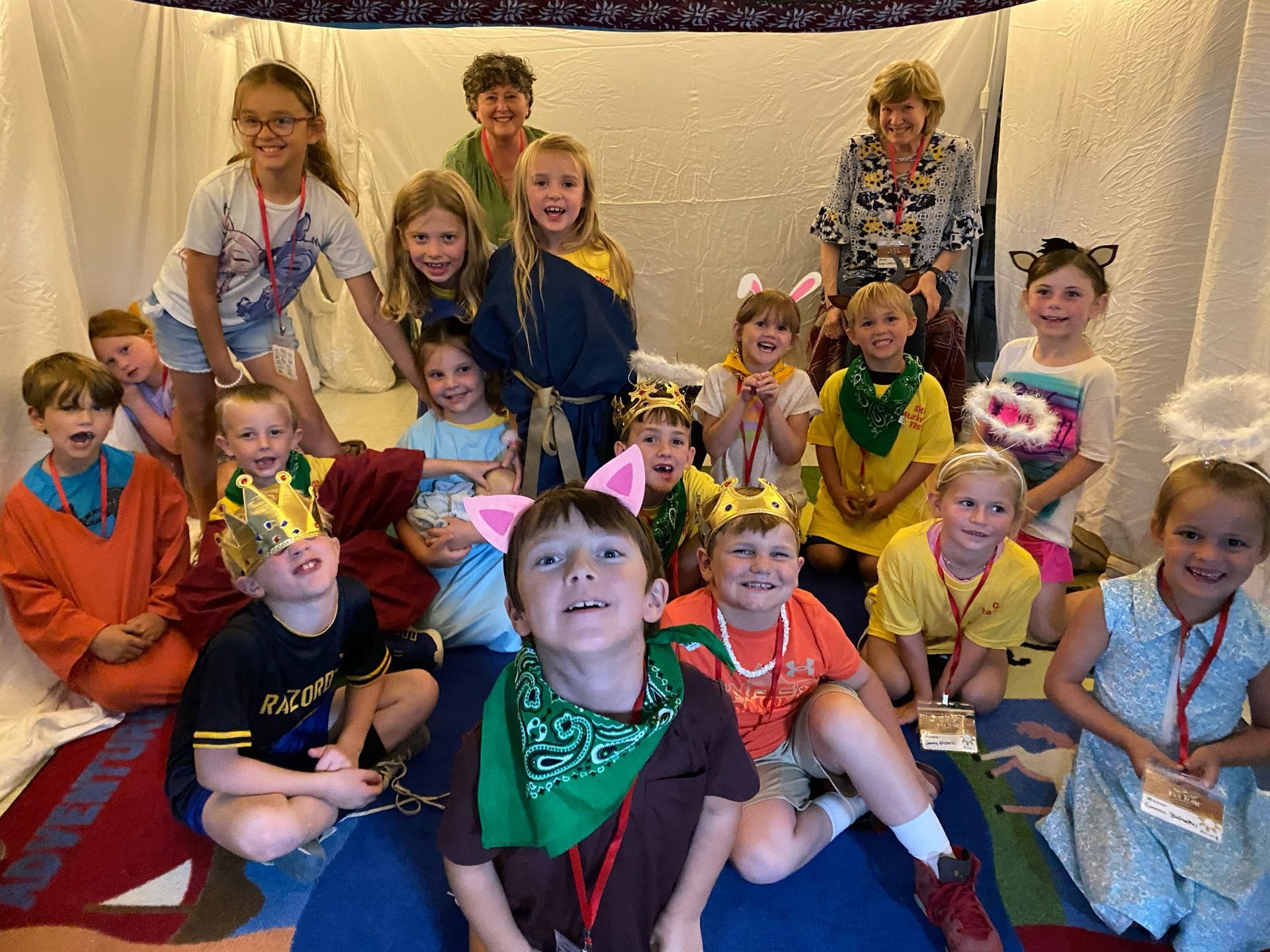 Group of children and two adults, smiling, posing for a photo. Many wear costumes, inside a decorated space.