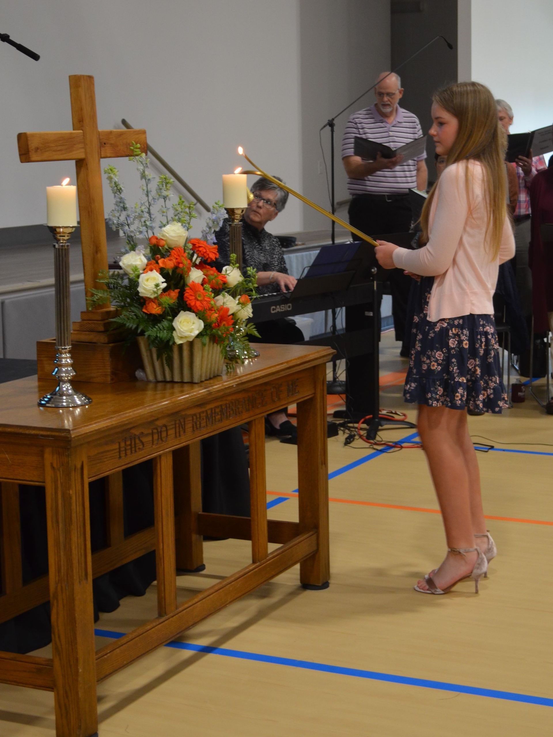 A girl stands in front of a wooden table with a cross on it