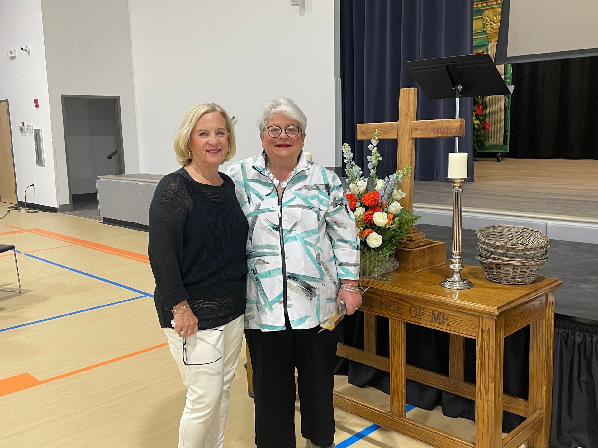 Two women are standing next to each other in front of a wooden cross.