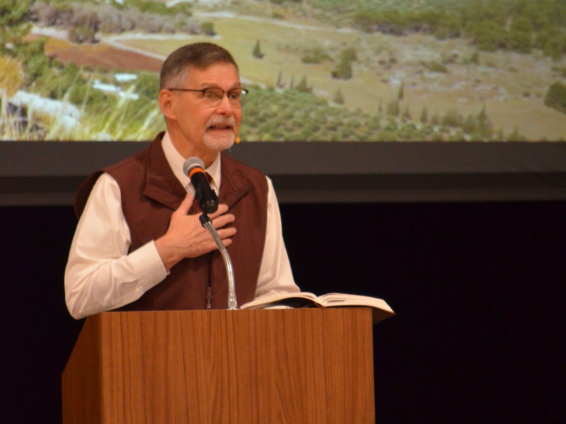 A man is standing at a podium holding a microphone and a bible.
