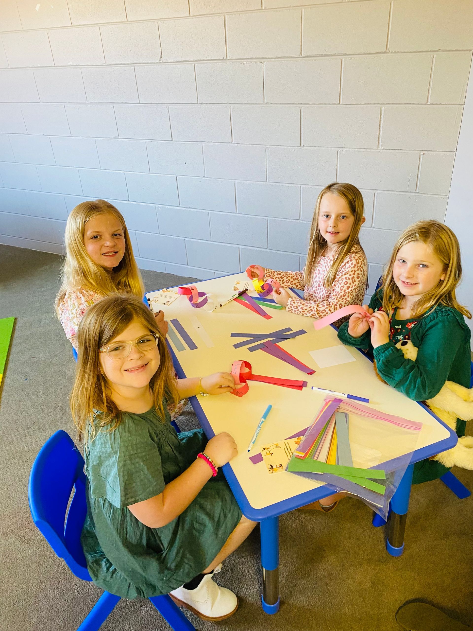 A group of young girls are sitting at a table making crafts.