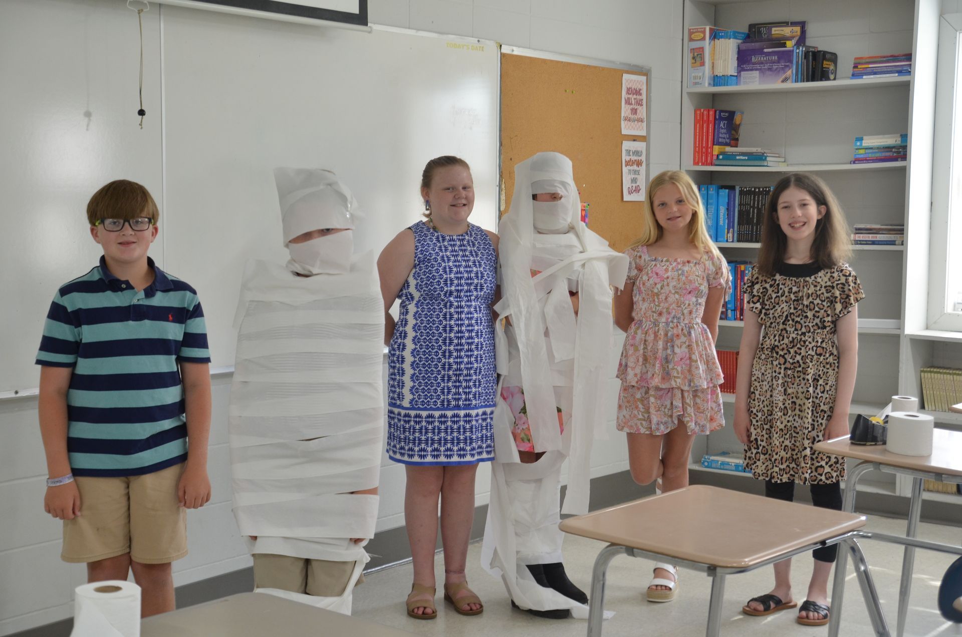 A group of children are wrapped in toilet paper in a classroom.