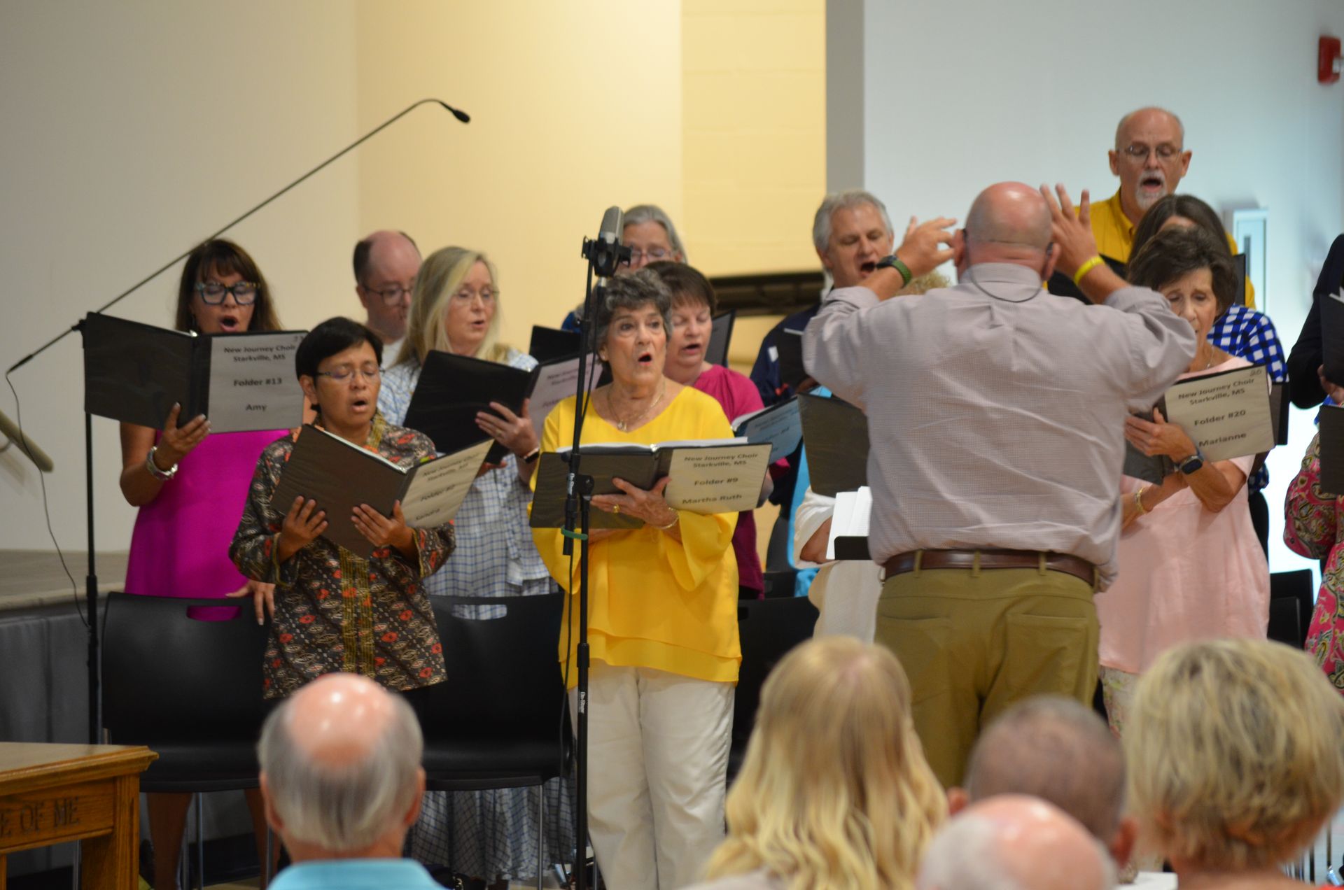 A group of people are singing in a choir in front of a crowd.