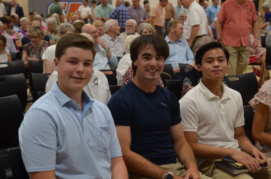 Three young men are sitting in front of a crowd of people.
