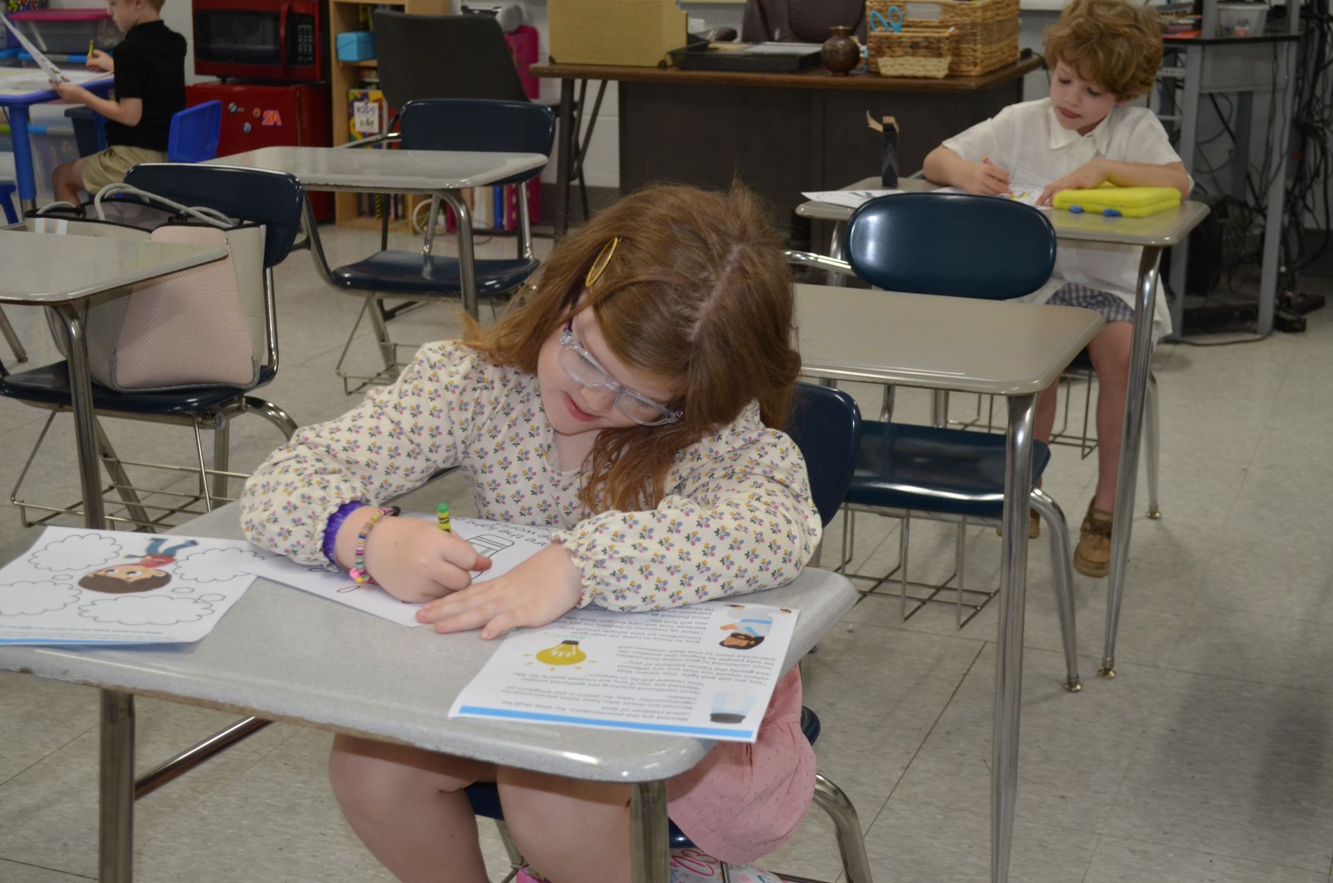 A girl is sitting at a desk in a classroom writing on a piece of paper.