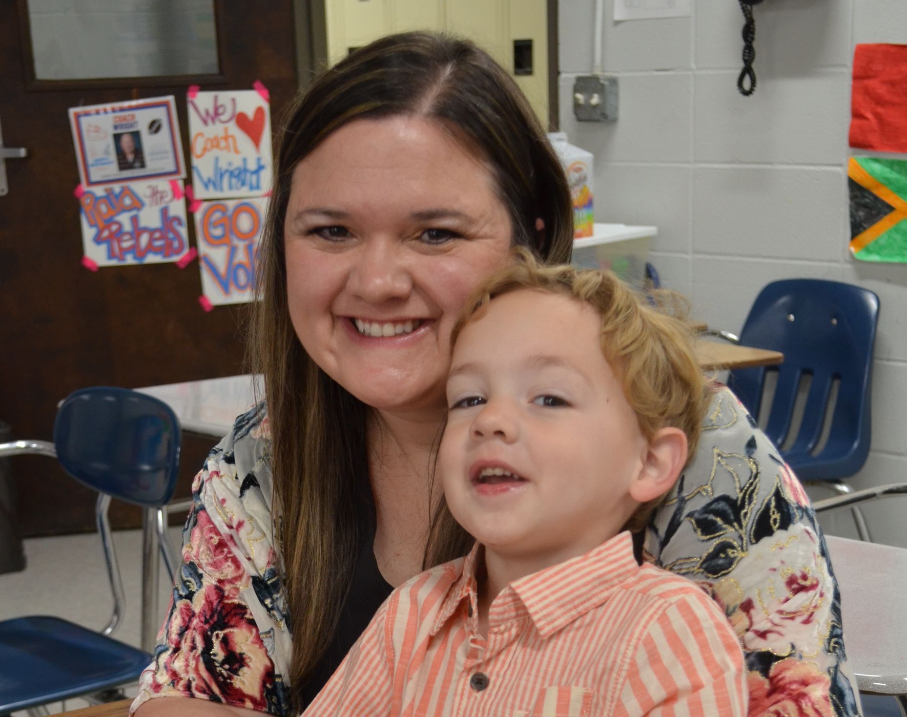 A woman is holding a little boy in her arms in a classroom.