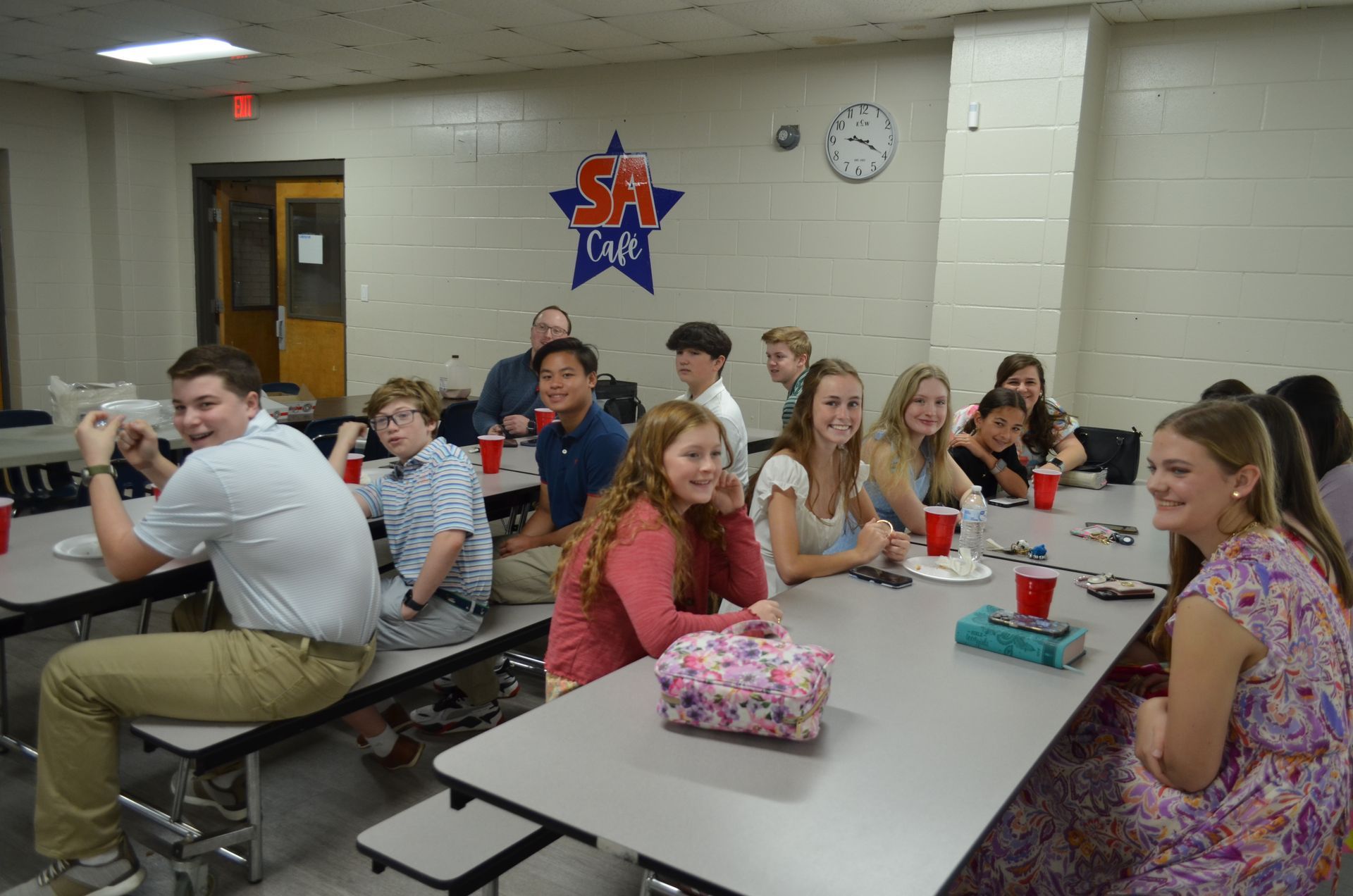 A group of people are sitting at long tables in a cafeteria.