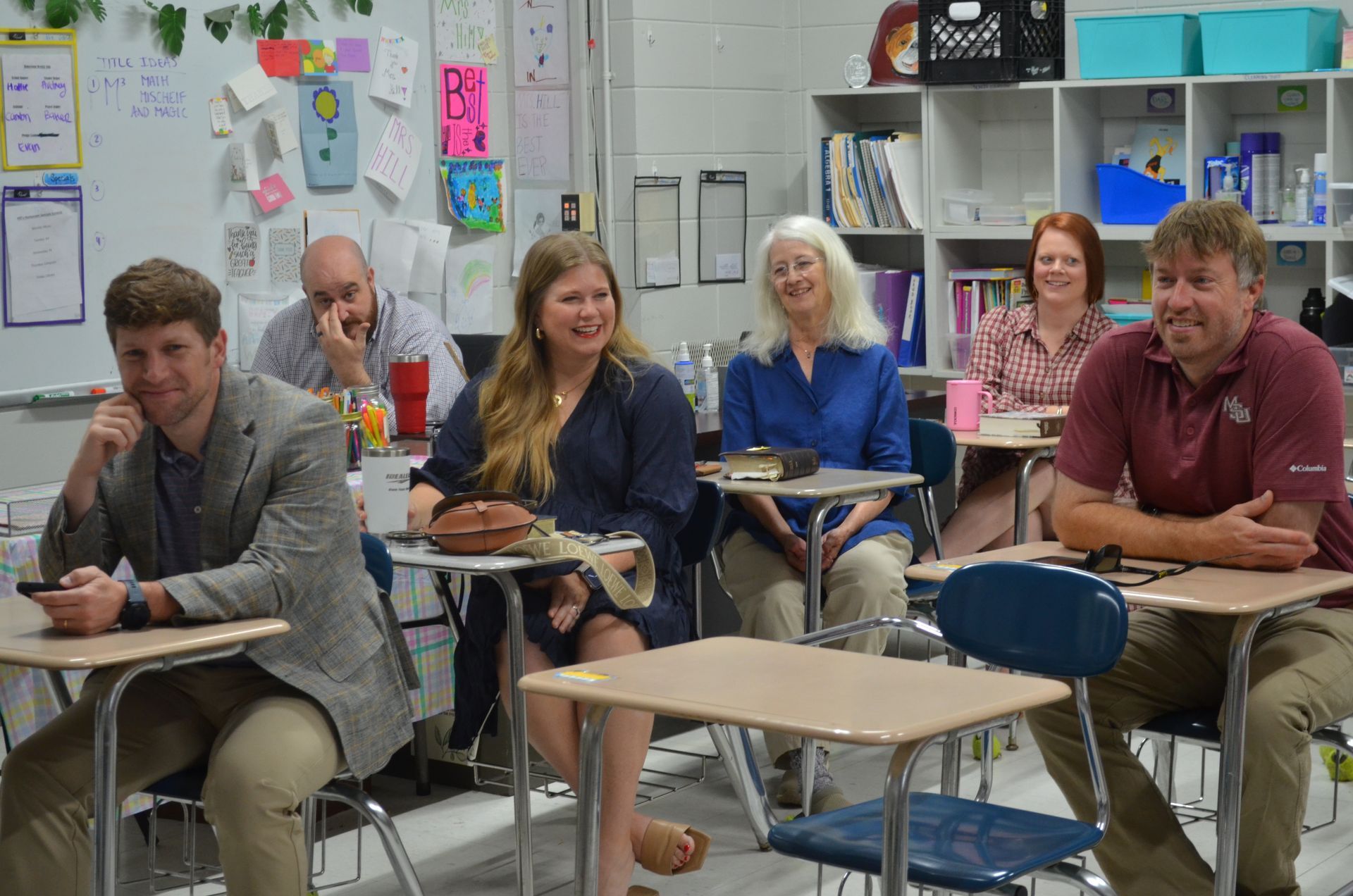 A group of people are sitting at desks in a classroom.
