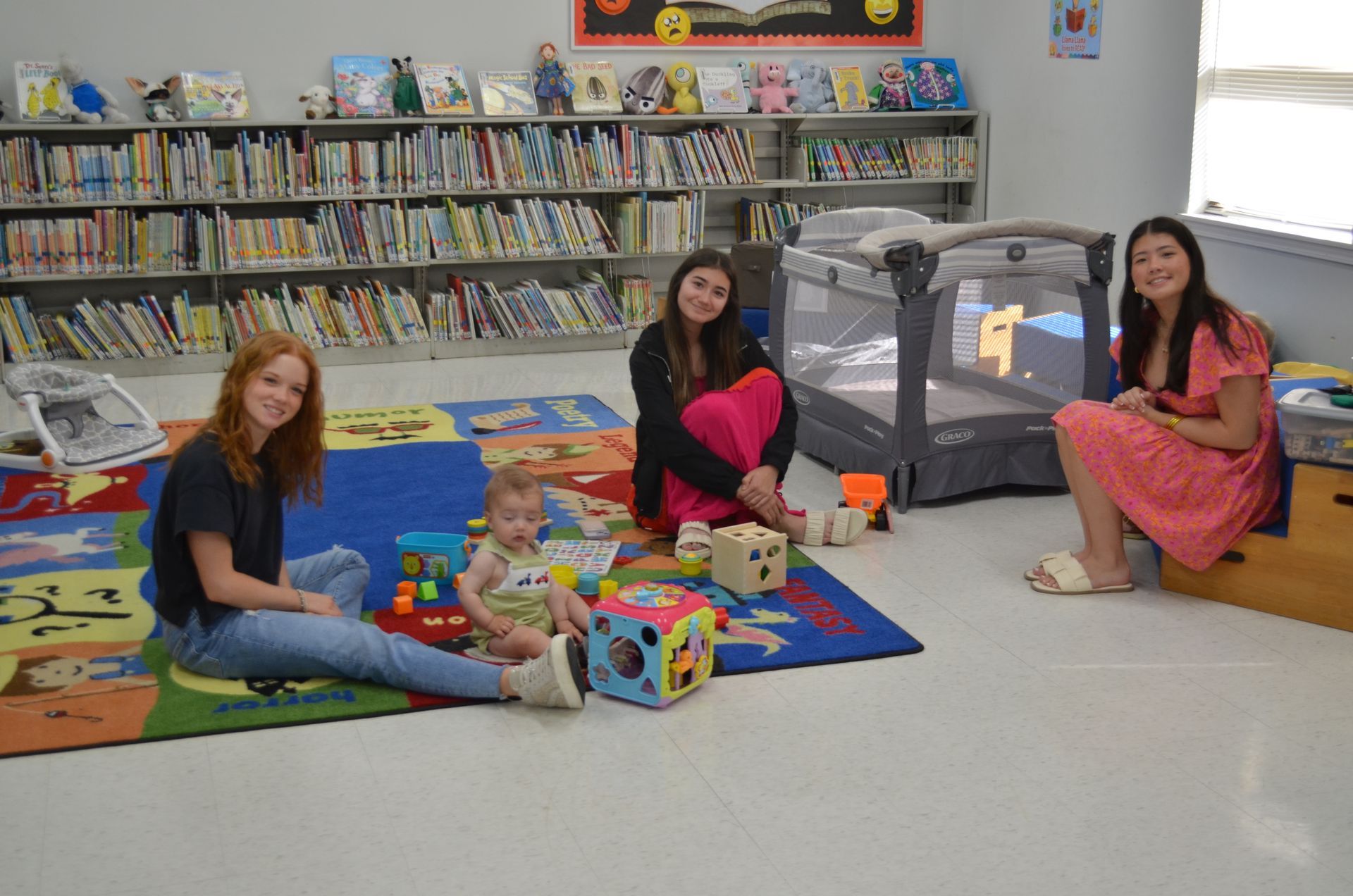 Three women are sitting on the floor with a baby and toys.