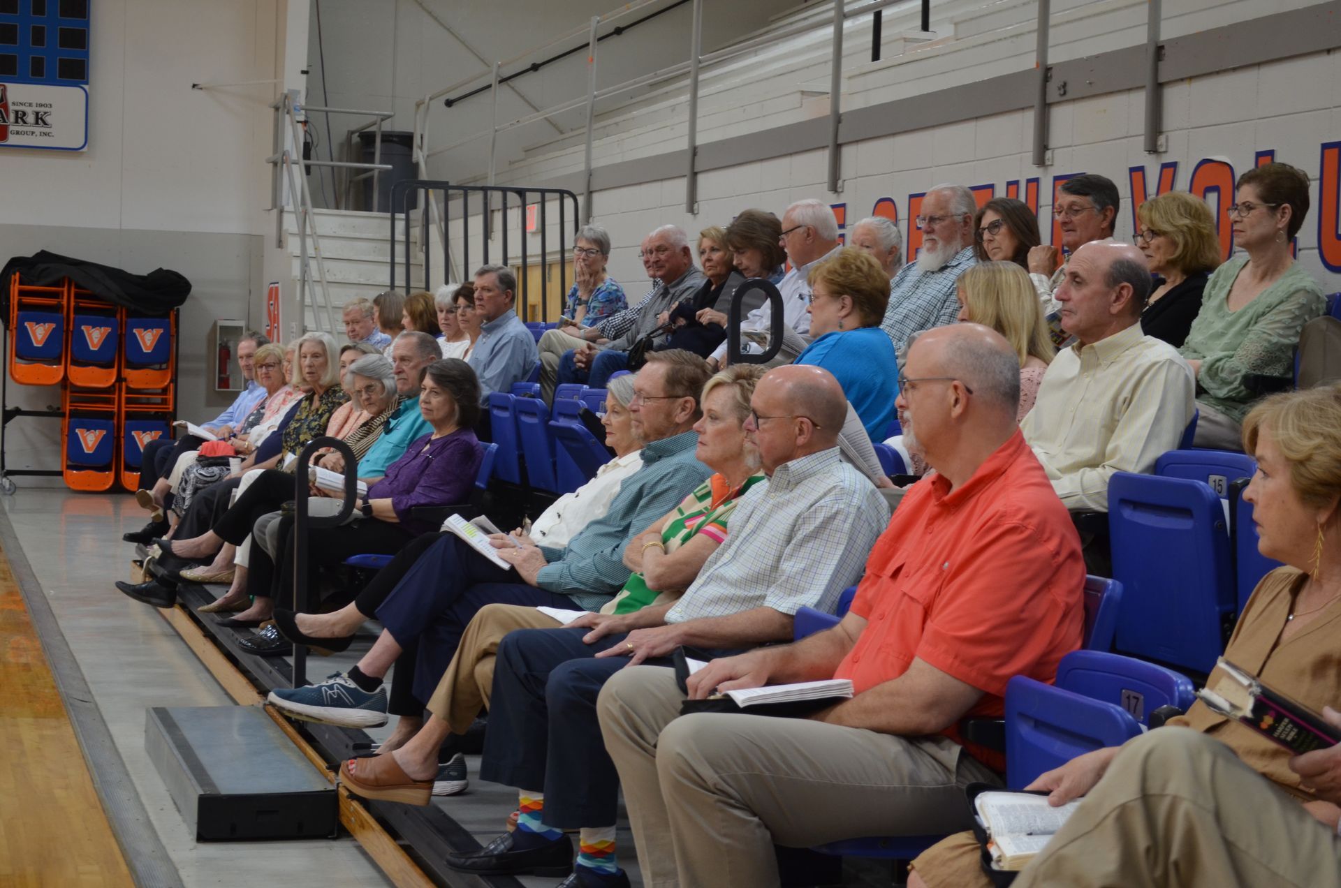 A large group of people are sitting in bleachers in a gym.