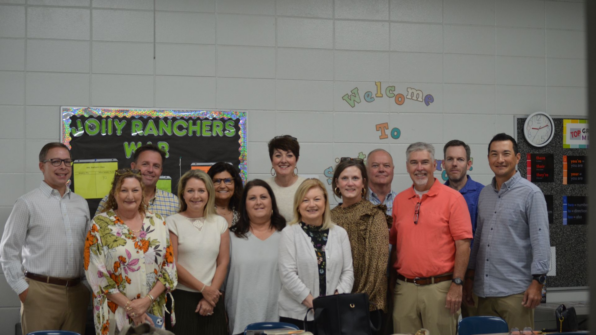 Group of people in a classroom; adults smiling for a photo in front of a bulletin board.